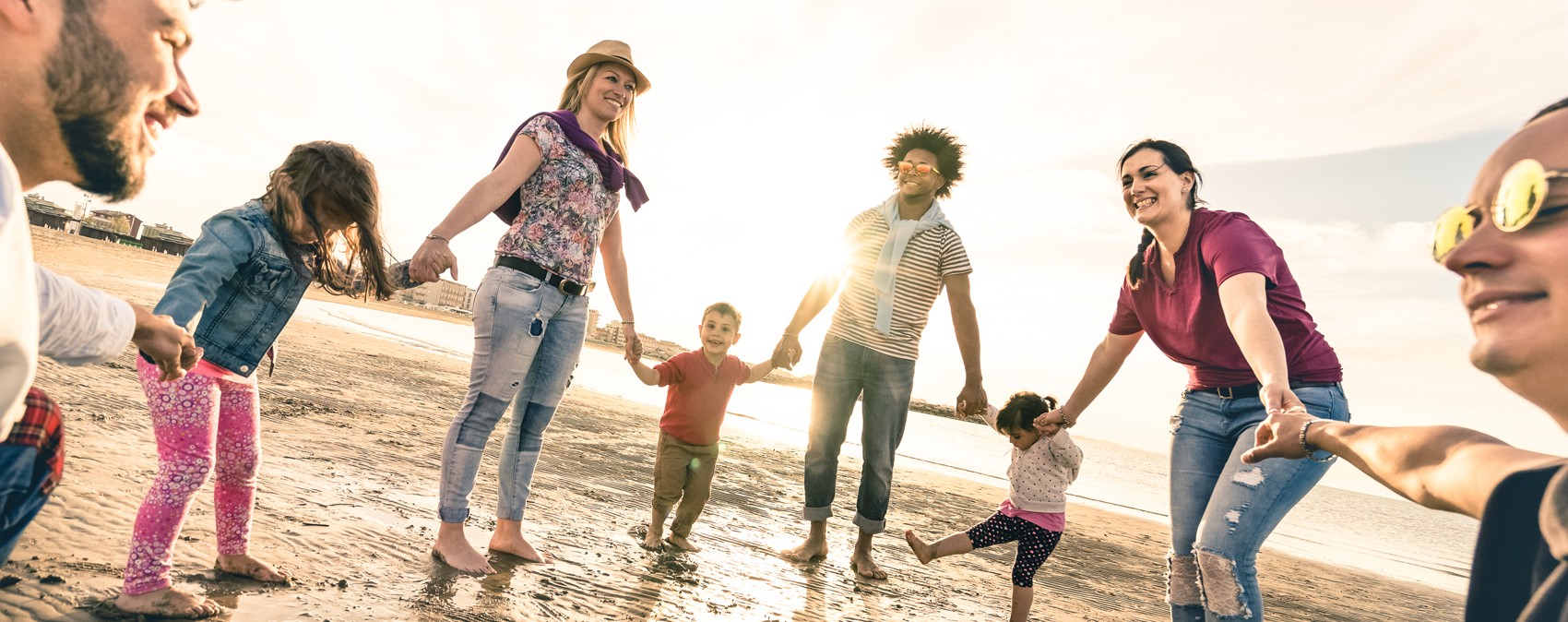 Mehrere Erwachsene und Kinder am Strand bei später Sonne geben sich gegenseitig die Hände